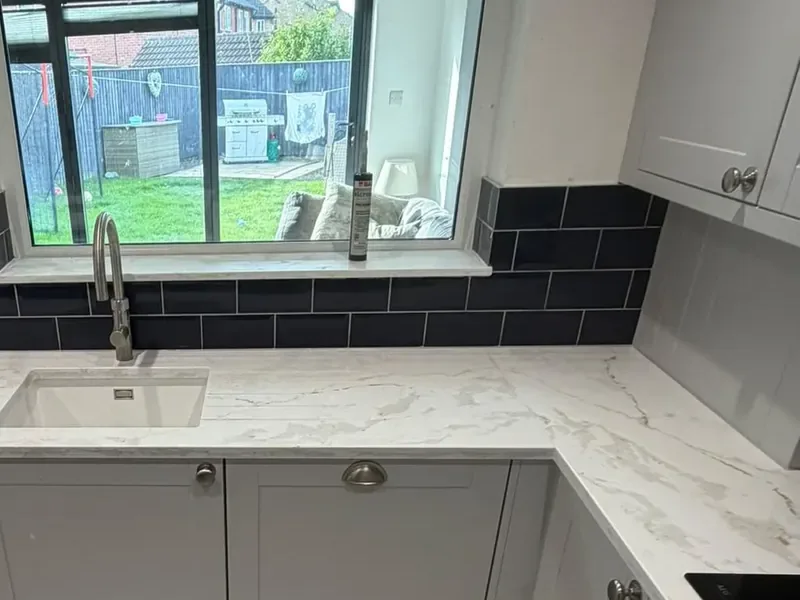 Navy metro tile splashback behind a white quartz worktop and sink