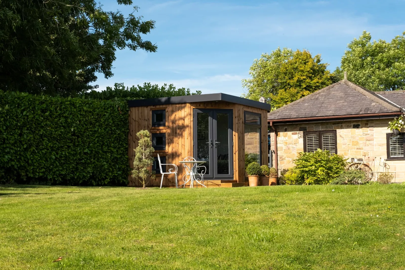 Timber-clad garden room with grey French doors in a lawned garden