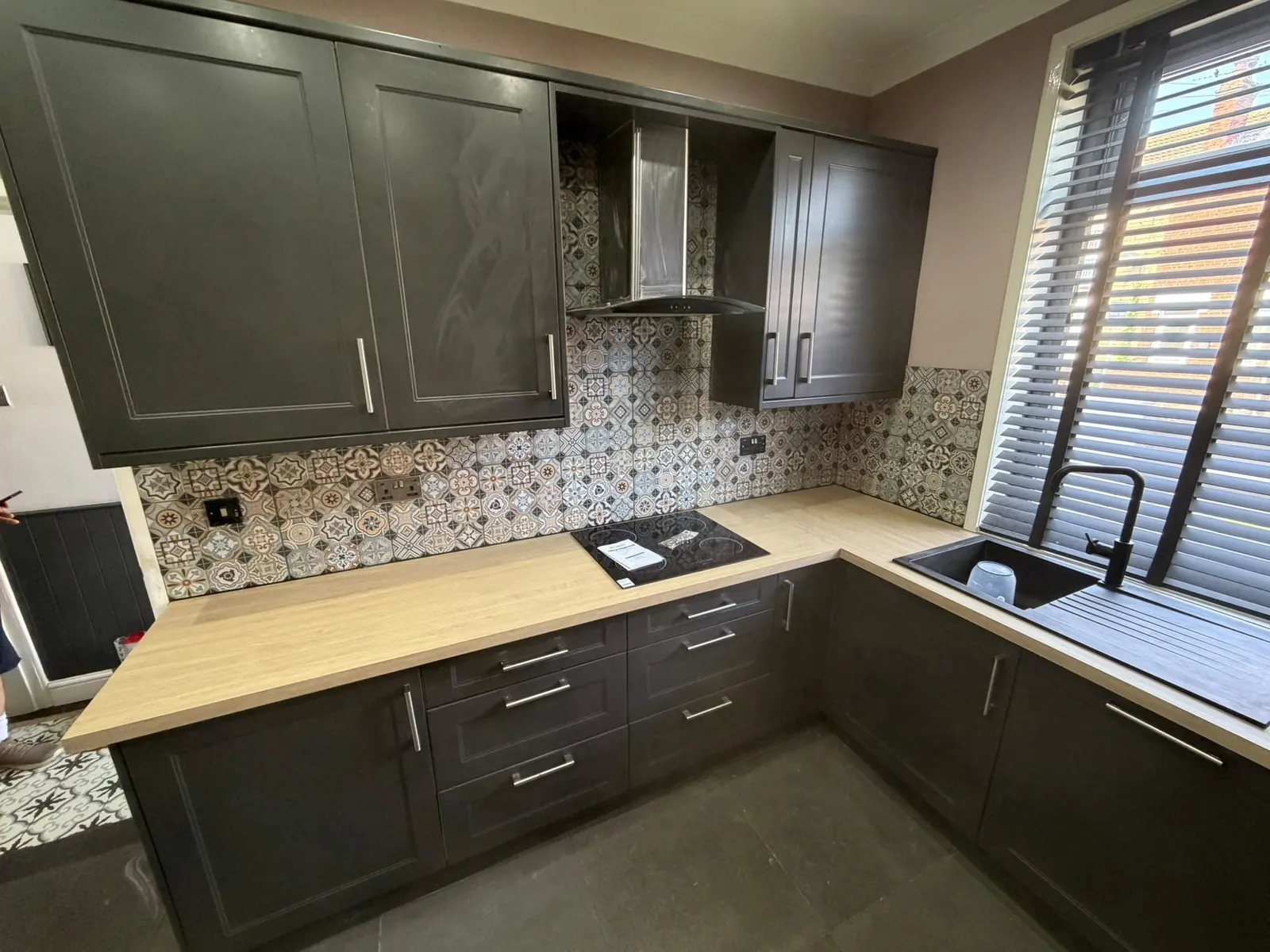 Patterned tile splashback in a dark grey kitchen with oak-effect worktops